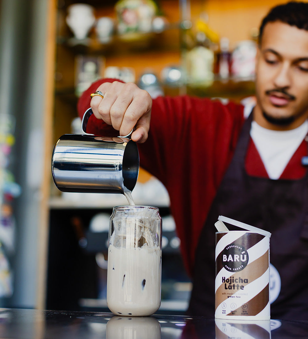 Hojicha Latte freddo in bicchiere con ghiaccio, preparato versando il latte – bevanda al tè verde tostato